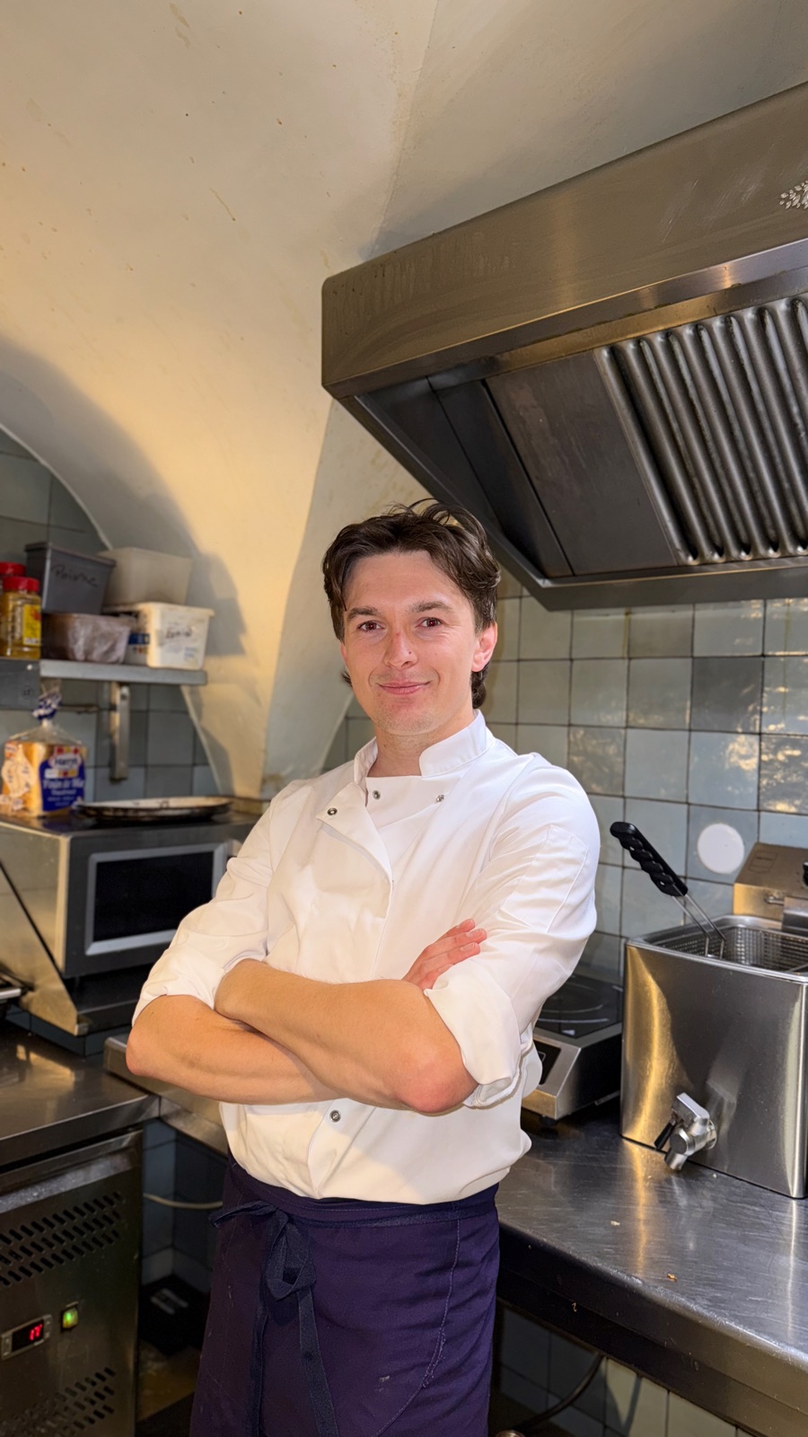 Arthur en tenue, bras croisés, dans une cuisine professionnelle